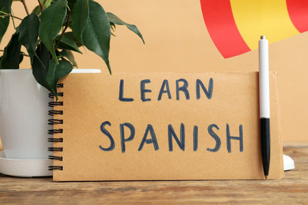 Notebook with text LEARN SPANISH, pen, houseplant and flag on table against beige backgroundの写真素材