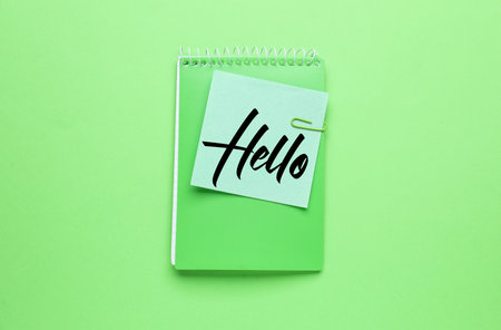 Sticky note with word HELLO and notebook on green backgroundの写真素材