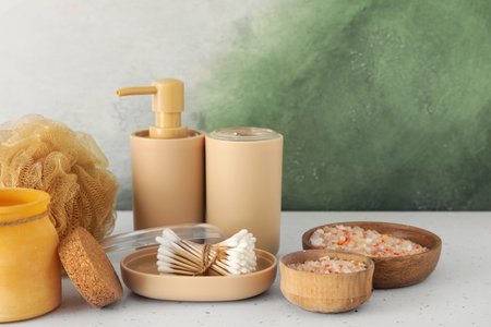 Bath accessories with bowls of sea salt on table near color wall