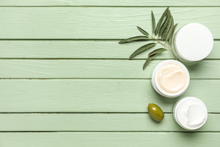 Jars of cream with olive and plant branch on green wooden backgroundの写真素材