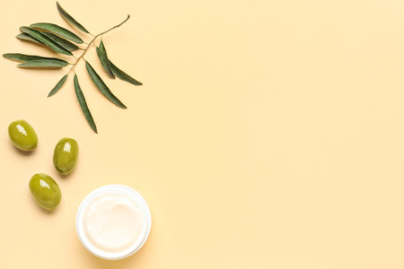 Jar of cream with green olives and plant branch on beige backgroundの写真素材