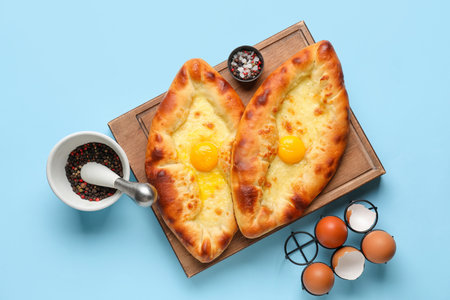 Wooden board with tasty Ajarian khachapuri, eggs and spices on color backgroundの写真素材