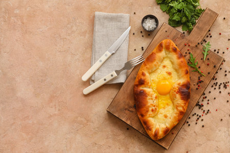 Wooden board with tasty Ajarian khachapuri and peppercorns on color background
