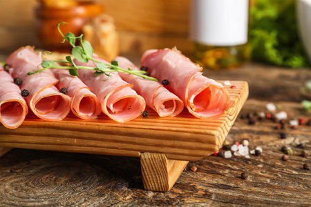 Board with rolled slices of tasty ham on wooden table, closeupの写真素材