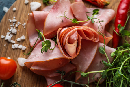 Wooden board with slices of tasty ham and microgreen, closeup