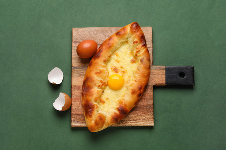 Wooden board with tasty Ajarian khachapuri on green backgroundの写真素材
