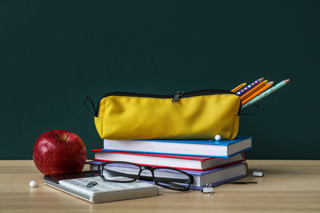 Pencil case with school stationery, apple and eyeglasses on table against dark backgroundの写真素材