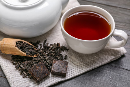 Napkin with scoop of dry puer tea, cup and teapot on dark wooden background, closeupの写真素材