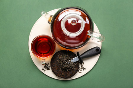 Dry pressed puer tea with knife, glass and teapot on green background
