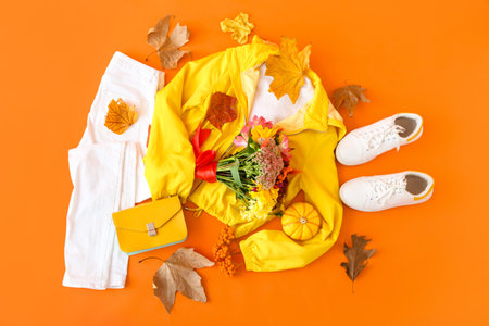 Stylish female outfit, bouquet of flowers and autumn decor on orange backgroundの写真素材