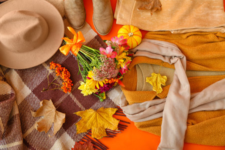 Warm female clothes, plaid, bouquet of flowers and autumn leaves on orange background