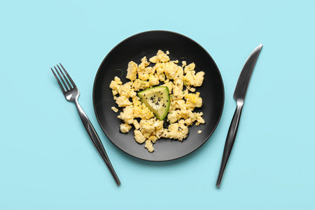Plate of tasty scrambled eggs and cutlery on color backgroundの写真素材