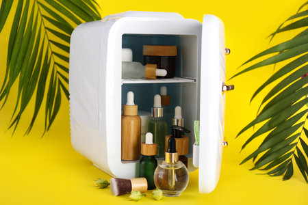 Small refrigerator with cosmetics and palm leaves on yellow backgroundの写真素材