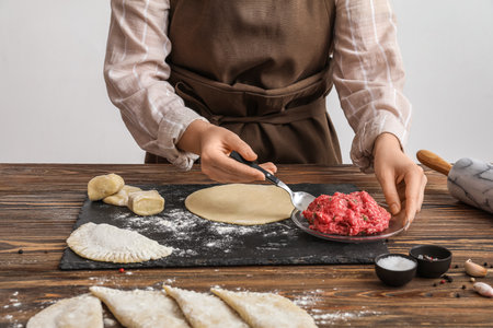 Woman taking spoon of mince while preparing cheburek at table near light wallの写真素材