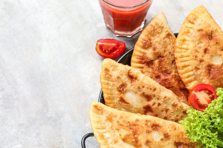 Frying pan with tasty chebureks on light background, closeup