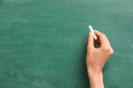 Female hand with chalk against green blackboardの写真素材