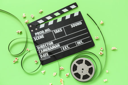 Movie clapper with reel and popcorn on green backgroundの写真素材