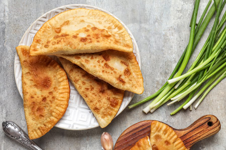 Plate with tasty chebureks and green onion on grunge backgroundの写真素材