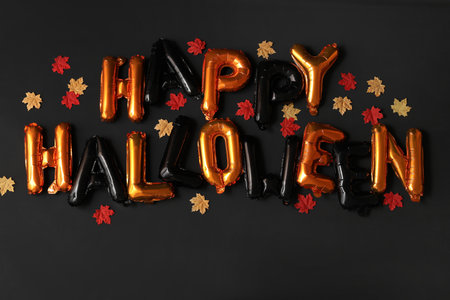 Text HAPPY HALLOWEEN made of foil balloons and leaves on dark backgroundの写真素材