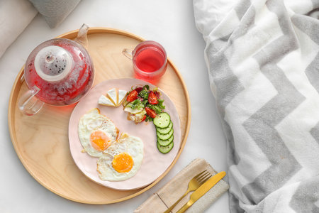 Wooden tray with tasty fried eggs and tea on bed, closeupの写真素材