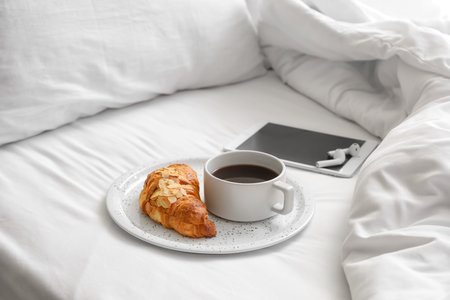 Plate with croissant and cup of aromatic coffee on bedの写真素材