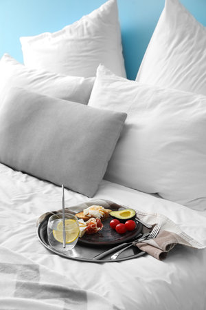 Tray with delicious breakfast and glass of water on bedの写真素材