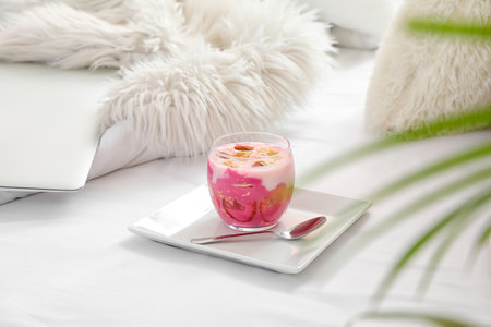 Glass of tasty yogurt with granola on comfortable bed