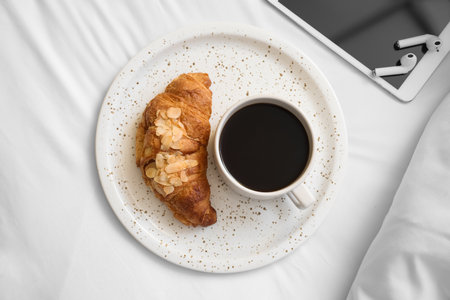 Plate with delicious croissant and cup of aromatic coffee on bedの写真素材