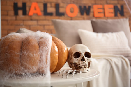 Human skull with skeleton hand and pumpkin on table in living room decorated for Halloween, closeupの写真素材