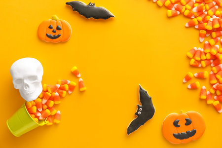 Frame made of Halloween candy corns, bucket, cookies and skull on yellow background