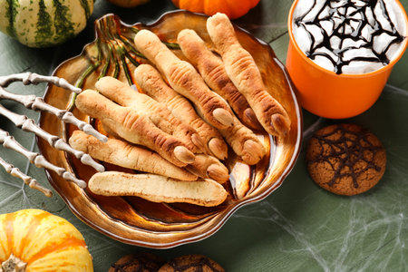 Plate with Halloween cookies, skeleton hand, drink and pumpkins on green wooden backgroundの写真素材