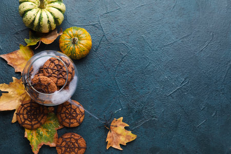 Glass bowl with Halloween spiderweb cookies, pumpkins and fallen leaves on dark backgroundの写真素材