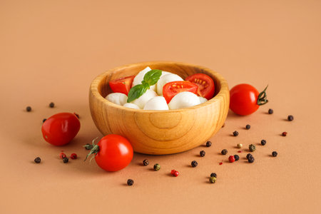 Bowl of delicious mozzarella cheese, tomatoes and spices on color backgroundの写真素材