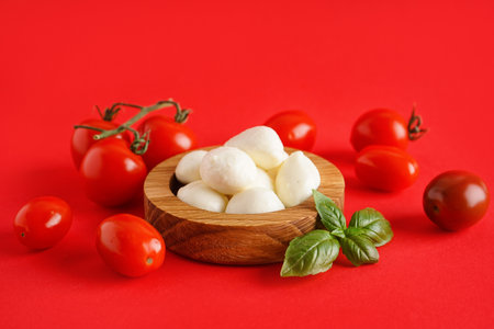 Wooden bowl with delicious mozzarella cheese and tomatoes on color backgroundの写真素材