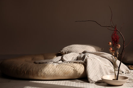 Bowl with beautiful ikebana, pillows and plaid on floor in dark room
