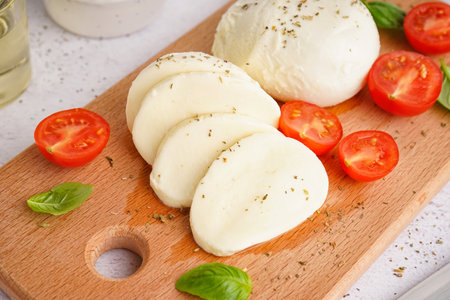 Wooden board with tasty mozzarella cheese and tomatoes on light background, closeupの写真素材