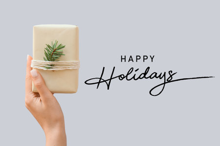 Female hand with Christmas gift on gray background. happy holidaysの写真素材