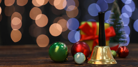 Golden Christmas bell and decorations on wooden table against blurred lightsの写真素材