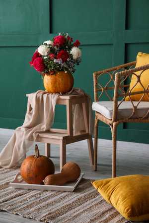 Pumpkin with beautiful flowers on stepladder, armchair and pillows near green wallの写真素材