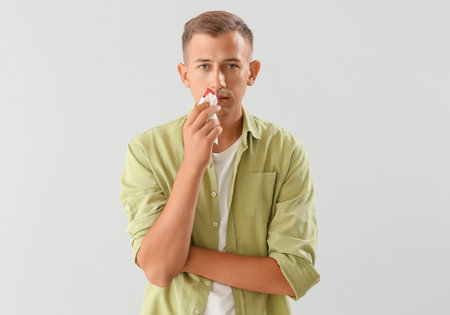 Young man with nosebleed and tissue on white backgroundの写真素材