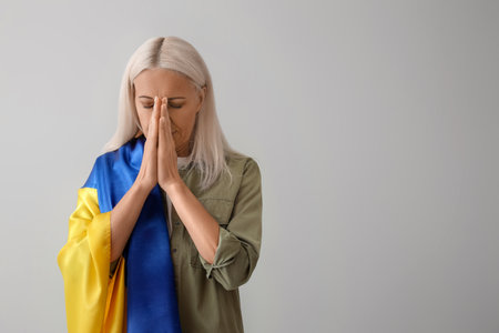 Mature woman with flag of Ukraine praying on light backgroundの写真素材