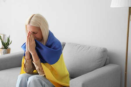 Mature woman with flag of Ukraine praying at homeの写真素材