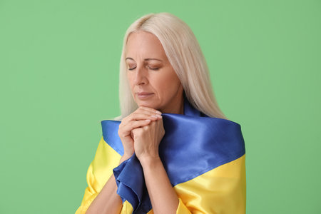 Mature woman with flag of Ukraine praying on green backgroundの写真素材