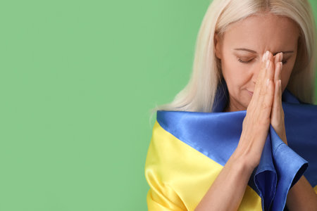 Mature woman with flag of Ukraine praying on green background, closeupの写真素材