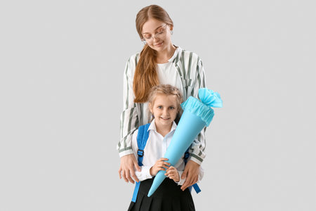 Cute little girl with blue school cone and her mother on light backgroundの写真素材