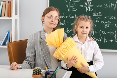 Cute little girl with school cone and teacher in classroomの写真素材