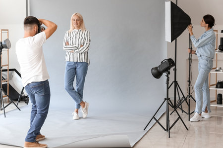 Male photographer and his assistant working with mature woman in studioの写真素材