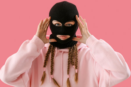 Portrait of young woman in balaclava touching face on pink backgroundの写真素材