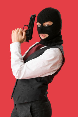 Young woman in balaclava posing with gun on red backgroundの写真素材