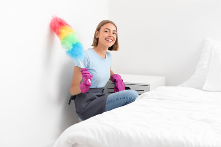 Young housewife with duster in bedroomの写真素材